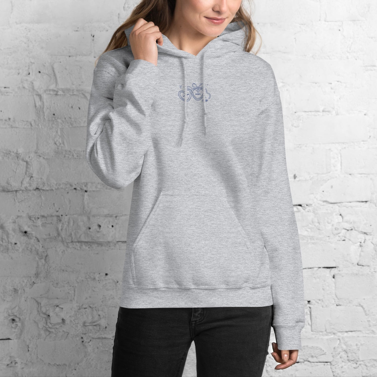 Woman wearing a gray bookish hoodie with a small logo against a white brick wall.