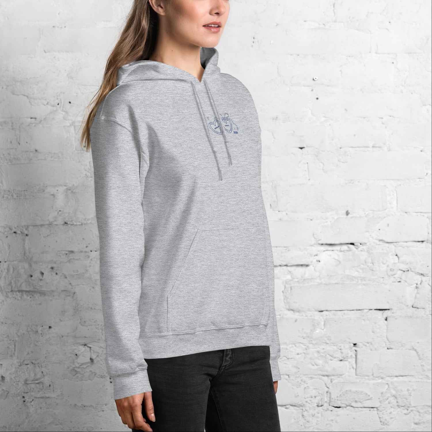 Woman wearing a gray bookish hoodie against a white brick wall