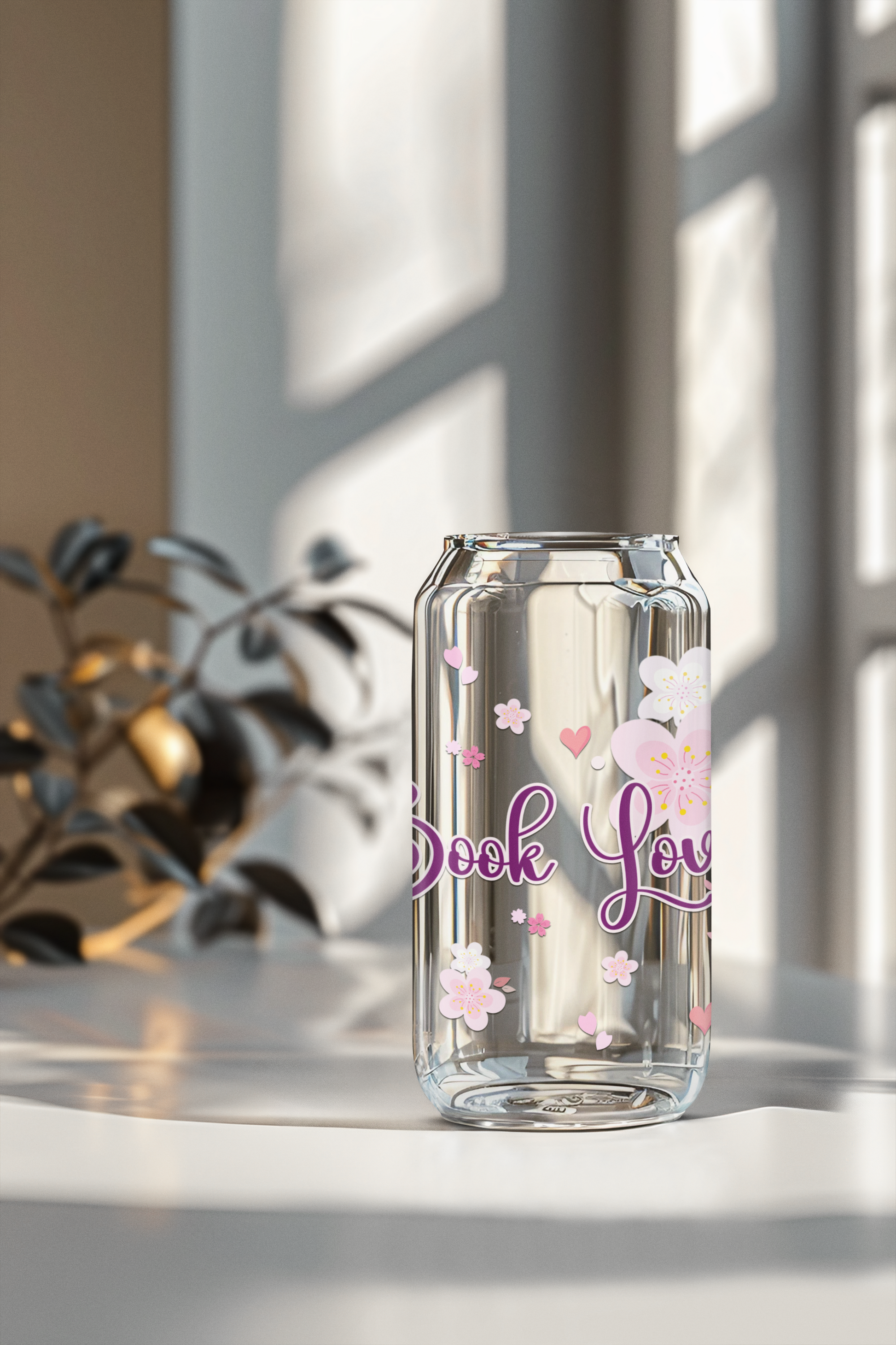 Clear bookish glass can with floral designs and book lover text on a light surface with a blurred background